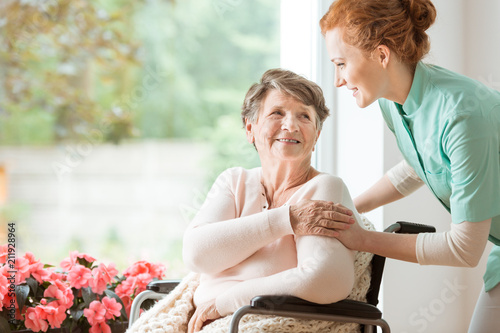 Young nurse helping an elderly woman in a wheelchair. Nursing home concept photo