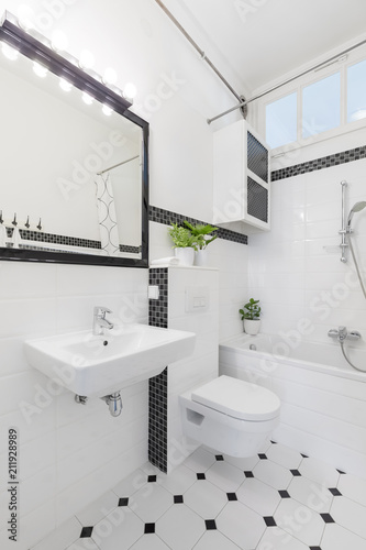 Mirror above washbasin in black and white bathroom interior with toilet and bathtub. Real photo