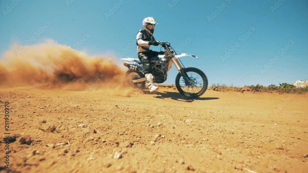 Motorcycler is riding through sand and raising clouds of dust Motorcycler is riding through sand and raising clouds of dust