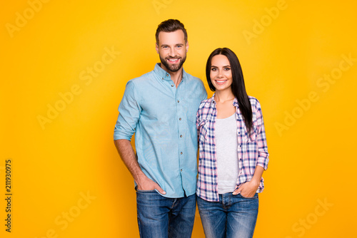 Portrait of attractive stylish couple hugging holding hands in pocket of pants looking at camera isolated on bright yellow background