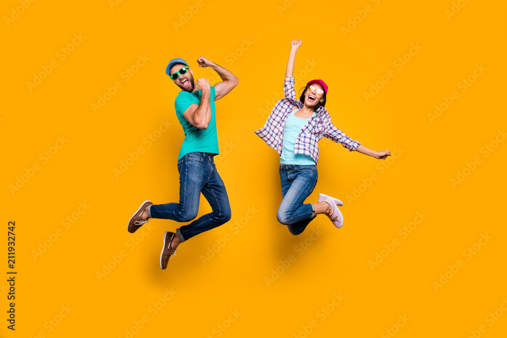 Portrait of funky active couple jumping with raised fists celebrating victory wearing casual clothes isolated on vivid yellow background