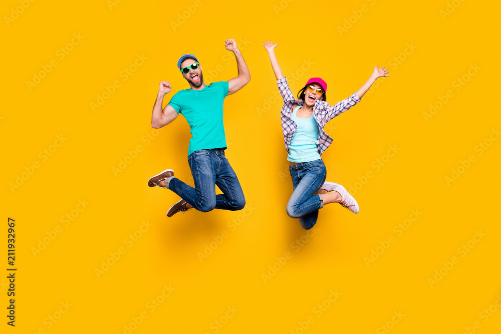 Portrait of lucky successful couple jumping with raised fists celebrating victory wearing denim outfit isolated on bright yellow background. Energy luck success concept - obrazy, fototapety, plakaty 