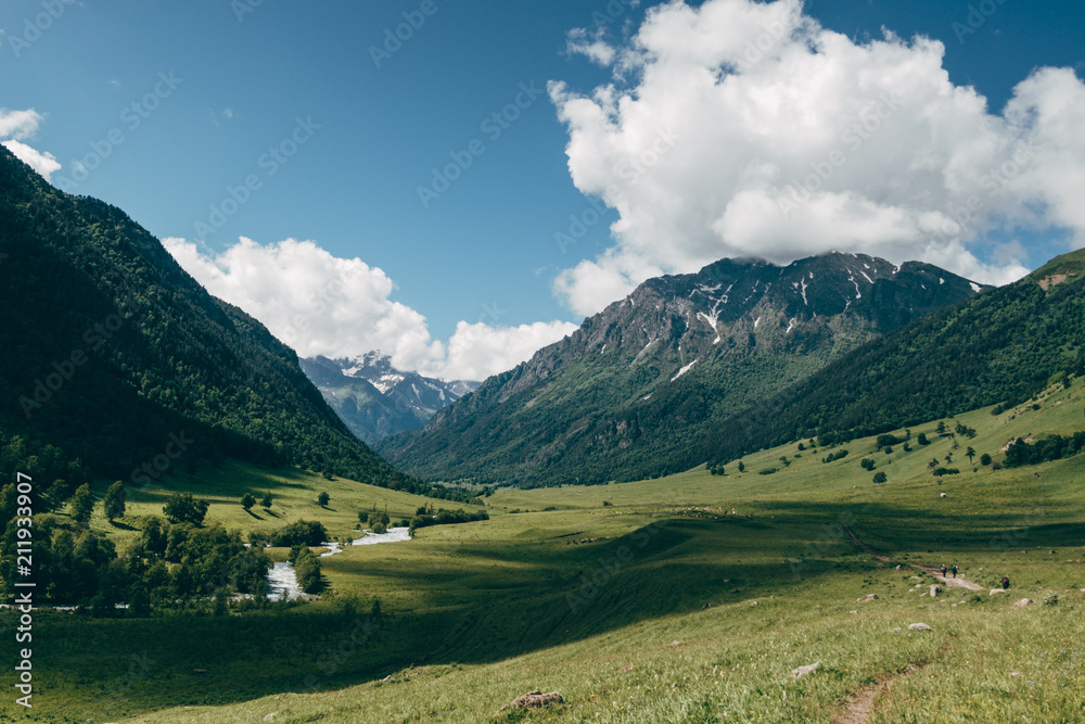 green mountain valley landscape with blue sky and white clouds. Deep shadows lies on a meadow