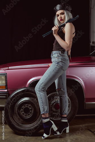 side view of beautiful stylish blonde woman in beret looking at camera while repairing car