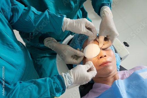 Valokuvatapetti Crop shot from above of careful surgeons applying patch with tape on eye of matu