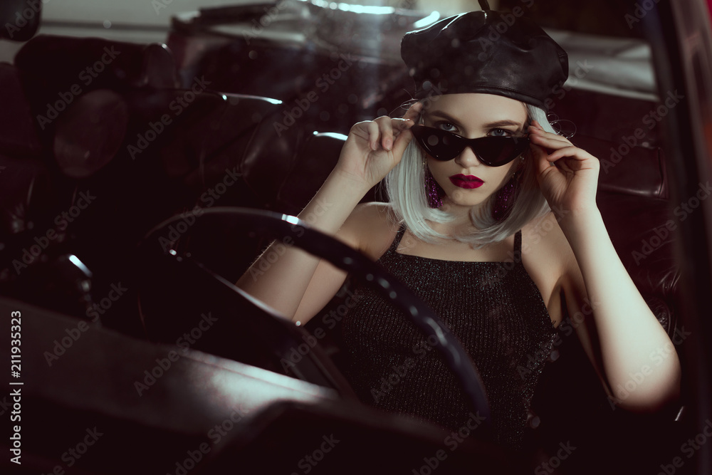 beautiful fashionable blonde girl in beret and sunglasses sitting in car and looking at camera beautiful fashionable blonde girl in beret and sunglasses sitting in car and looking at camera