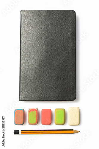 Pencil, eraser and notebook on white background. Close up of a wooden pen orange and black, an multicolor erasers and a booklet black. A diary with instruments for writing