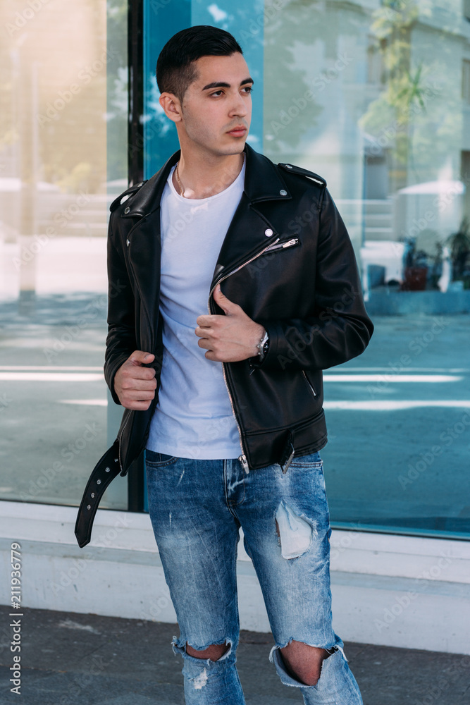 Obraz premium young, beautiful and attractive guy is standing near the glass building the city, posing.