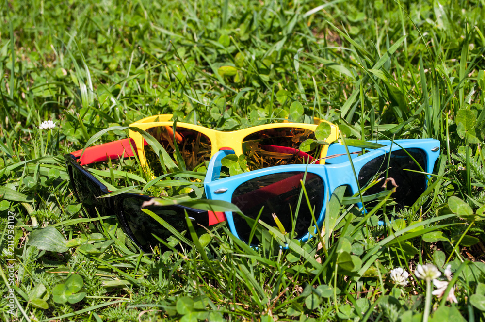 Blue red and yellow sunglasses in the green grass with mobile phone
