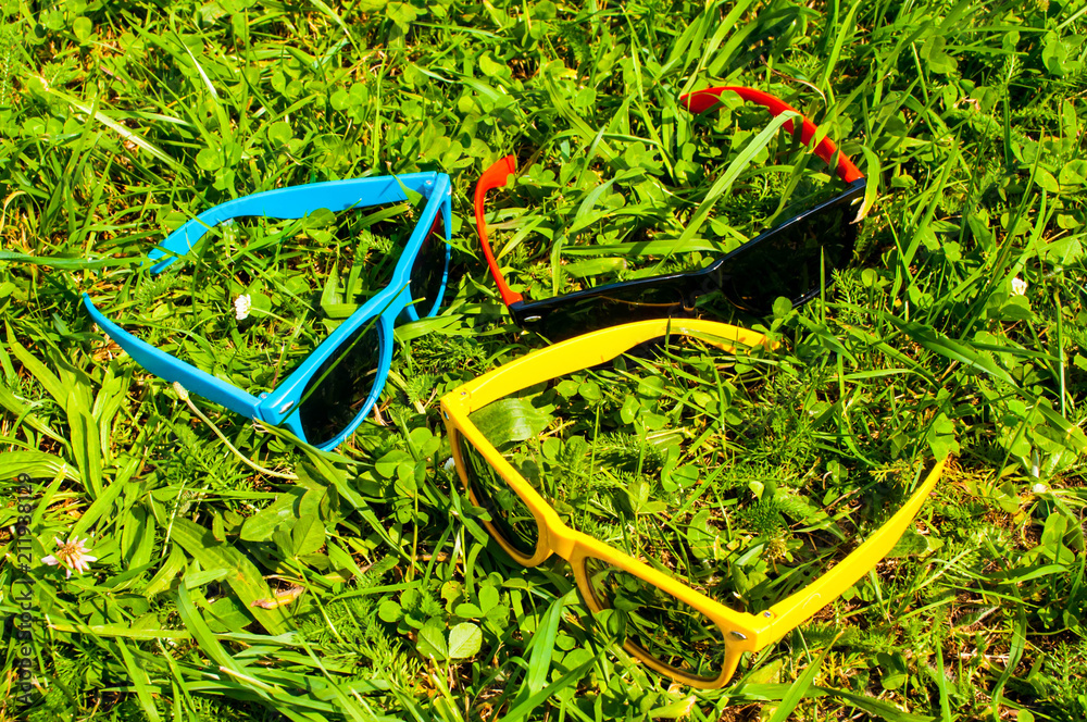 Blue red and yellow sunglasses in the green grass with mobile phone Blue red and yellow sunglasses in the green grass with mobile phone