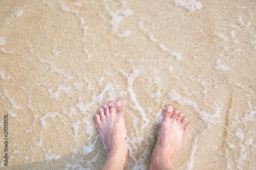 Closeup of a man's bare feet stand at wet on the beach , with a wave's edge foaming gently beneath them. Vacation on ocean beach, foot on sea sand. Leave empty copy space Enter the text above.