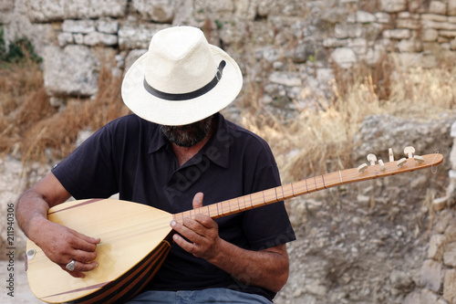 A street musician plays a Turkish instrument. A man in a white hat plays a game of baglama. photo