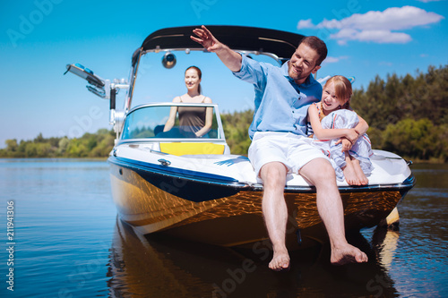 Interesting stories. Cheerful young father pointing at riverbanks and telling his little daughter stories while they sitting on the bow of the boat