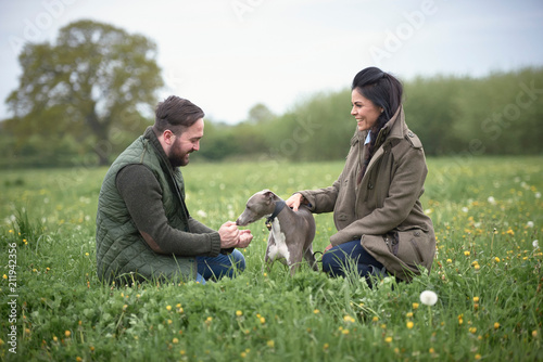 Woman and man kneeling to pet dog in field photo