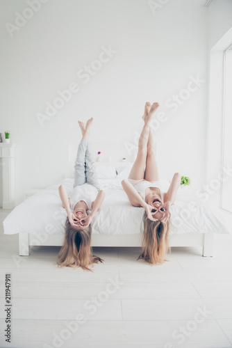 Wallpaper Mural Indoors domestic life mom mum mommy motherhood concept. Vertical full length body size view photo of beautiful cute cheerful joyful girls lying upside down on white bed in light modern room Torontodigital.ca