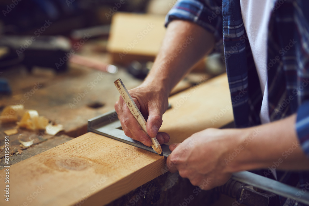A carpenter uses a framing square. A man works in a carpentry shop.