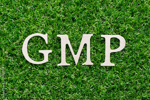 Wood alphabet in word GMP (abbreviation of Good manufacturing pracice)on artificial green grass background