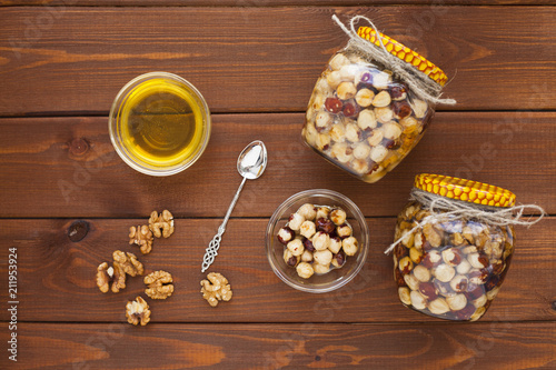 Natural honey and nuts in glass jars, vintage silver spoon on the wooden background. Healthy food, diet, lifestyle concept. Top view. Close up.