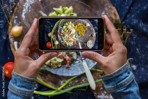 Woman hands take smartphone food photo of raw vegan zucchini spaghetti. Phone food photography for social media or blogging in popular and trendy top view style. Raw vegan vegetarian meal concept.