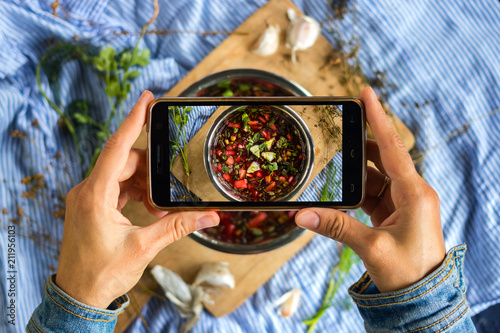Woman hands take smartphone food photo of cherry cold chrianteli soup. Phone food photography for social media or blogging in popular and trendy top view style. Raw vegan vegetarian meal concept.