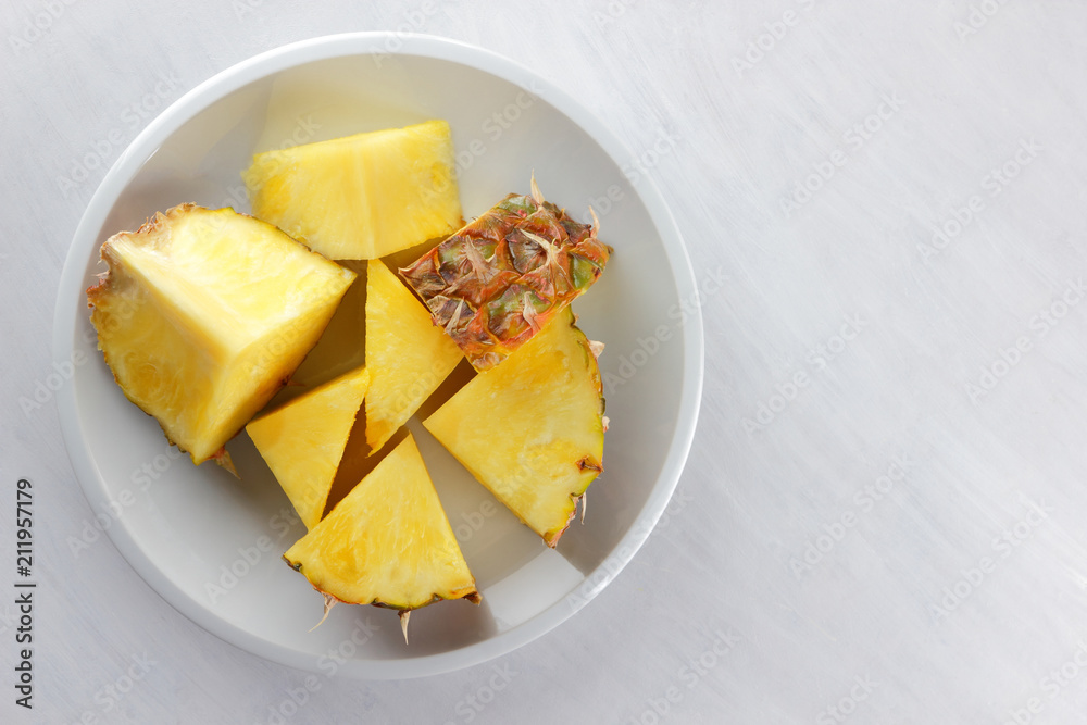 Pieces of pineapple on a white plate, pineapple on a white background top view, salad of tropical fruits for breakfast, vegetarian food, copy space Pieces of pineapple on a white plate, pineapple on a white background top view, salad of tropical fruits for breakfast, vegetarian food, copy space