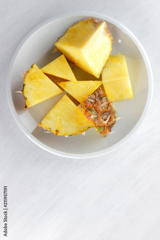 Pieces of pineapple on a white plate, pineapple on a white background top view, salad of tropical fruits for breakfast, vegetarian food, copy space Pieces of pineapple on a white plate, pineapple on a white background top view, salad of tropical fruits for breakfast, vegetarian food, copy space