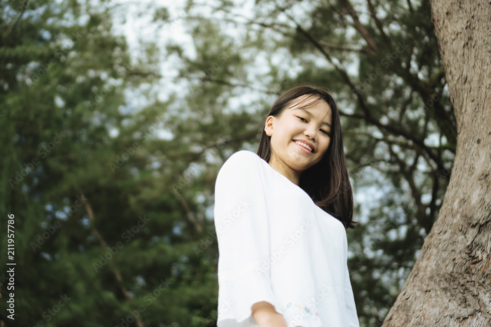 Young Asian woman smiling while standing against tree branches background. View from bottom. Young Asian woman smiling while standing against tree branches background. View from bottom.