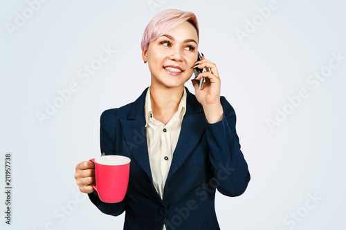 Young business woman holds cup of coffee and speaks on a smartphone, isolated on blue background