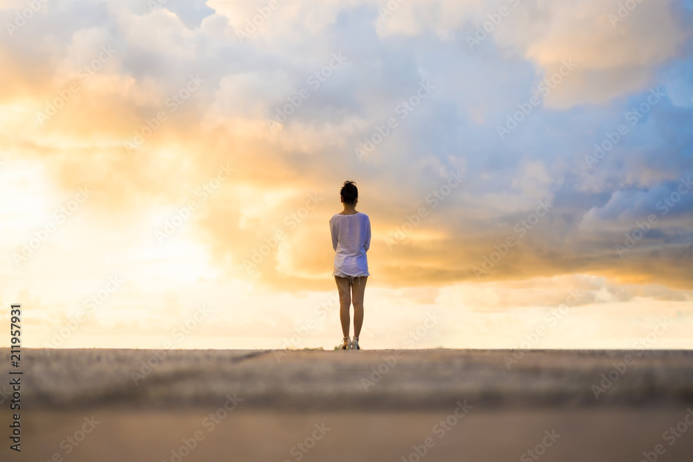 Woman looking at beautiful dramatic cloudy sky during sunset. - obrazy, fototapety, plakaty 