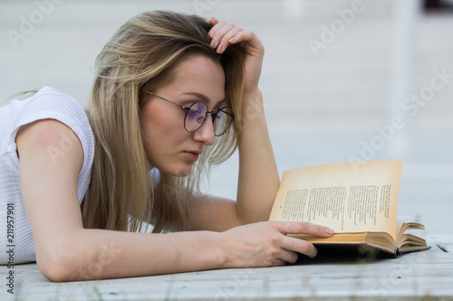 Portrait of young woman reading a book lying on the bench in the park