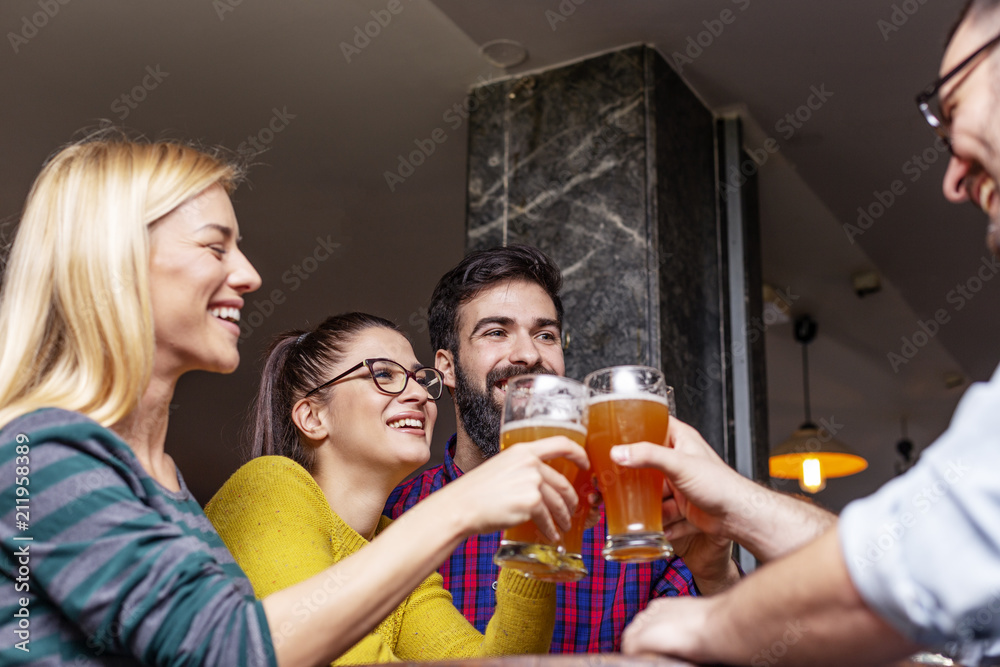 Group of four people toasting with glasses full of beer in local pub Group of four people toasting with glasses full of beer in local pub