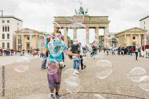 Street performer, busker, entertaining the crowd in front of the Brandenburg Gate in Berlin on an overcast summer day. Colorful soap bubbles floating in the foreground.