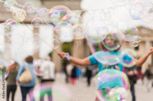 Street performer, busker, entertaining the crowd in front of the Brandenburg Gate in Berlin on an overcast summer day. Colorful soap bubbles floating in the foreground.