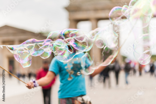 Street performer, busker, entertaining the crowd in front of the Brandenburg Gate in Berlin on an overcast summer day. Colorful soap bubbles floating in the foreground.