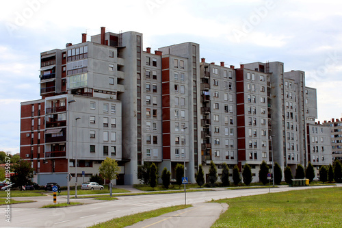 Old industrial looking concrete apartment building with multiple apartments on each floor and many windows in different sizes with grass area and road right in front of it
