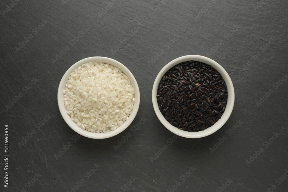 Dos cuencos blancos con arroces diferentes, blanco redondo y negro sobre un fondo negro de piedra Dos cuencos blancos con arroces diferentes, blanco redondo y negro sobre un fondo negro de piedra
