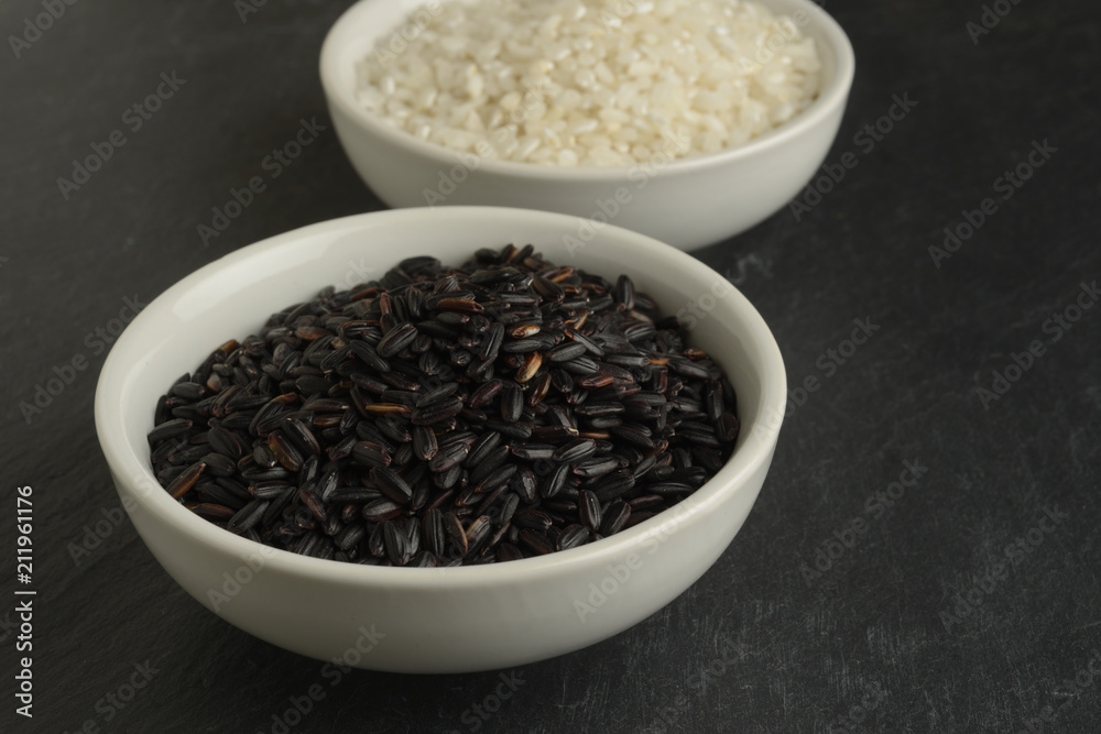 Dos cuencos blancos con arroces diferentes, blanco redondo y negro sobre un fondo negro de piedra Dos cuencos blancos con arroces diferentes, blanco redondo y negro sobre un fondo negro de piedra