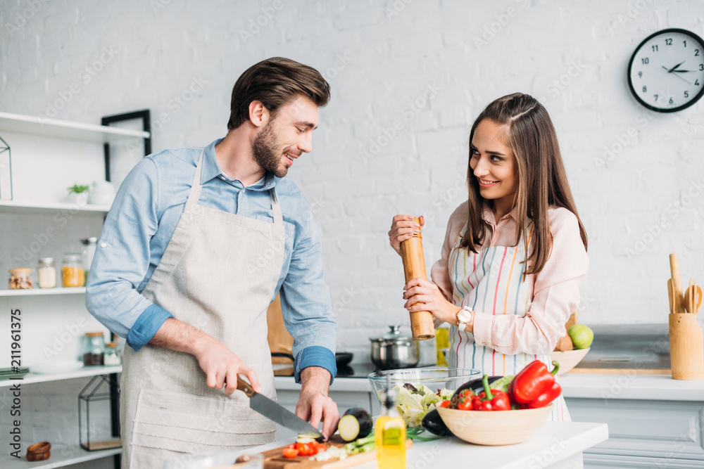 boyfriend cutting vegetables and girlfriend adding spices to salad in kitchen boyfriend cutting vegetables and girlfriend adding spices to salad in kitchen