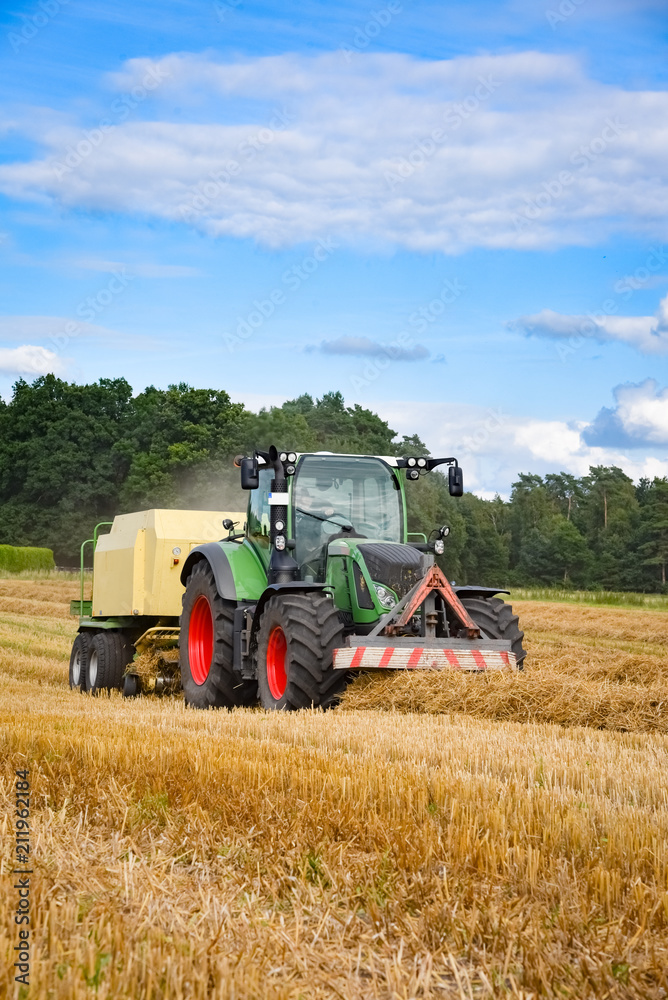 Obraz premium Strohernte - Traktor mit Strohpresse, Hochformat