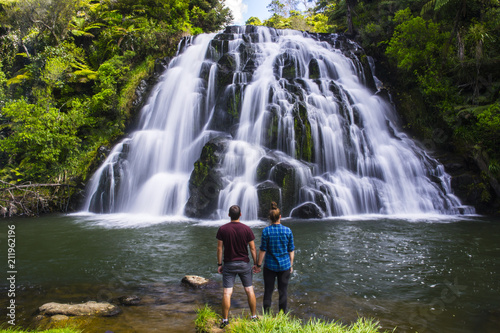 Travel New Zealand. Young tourist couple/friends overlooking waterfall. Popular tourist attraction in North Island. Long exposure falling water. Summer holidays. Natural, outdoor, travel background.