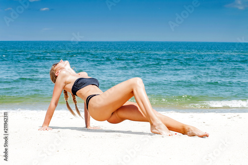 Beautiful slim woman in bikini lying on sand on the beach