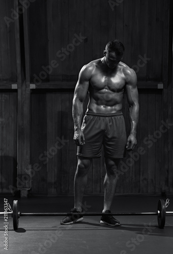 Healthy sporty man preparing for training and looking at barbell, black and white image