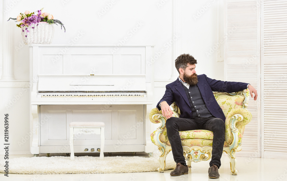 Macho attractive and elegant on serious face and thoughtful expression. Elite lifestyle concept. Man with beard and mustache wearing classic suit, sits on old fashioned armchair in luxury interior.