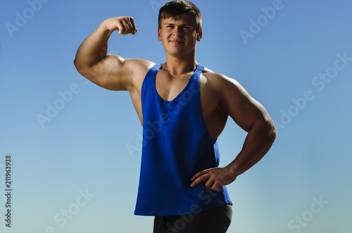 the athlete on the beach posing on blue sky background. Strong hands