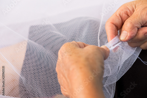 The old sewer woman is sewing fabric with needle to make net for protect her children from mosquito
