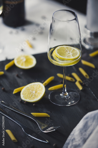 Wine glasses of home lemonade for italian dinner with pasta and peper on the grey wooden background and two kind of textile
