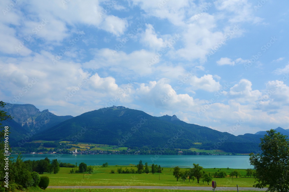 Lake called Wolfgangsee in Austria with mountains in the background and clouds on the sky and grass in the front