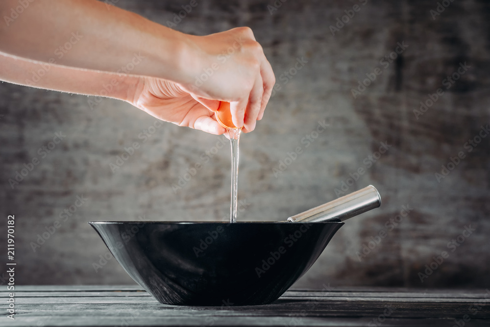 chef breaks eggs into black bowl on wooden table chef breaks eggs into black bowl on wooden table