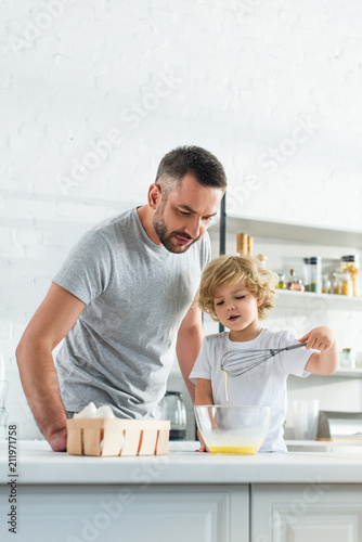 father with son whisking eggs in bowl at kitchen