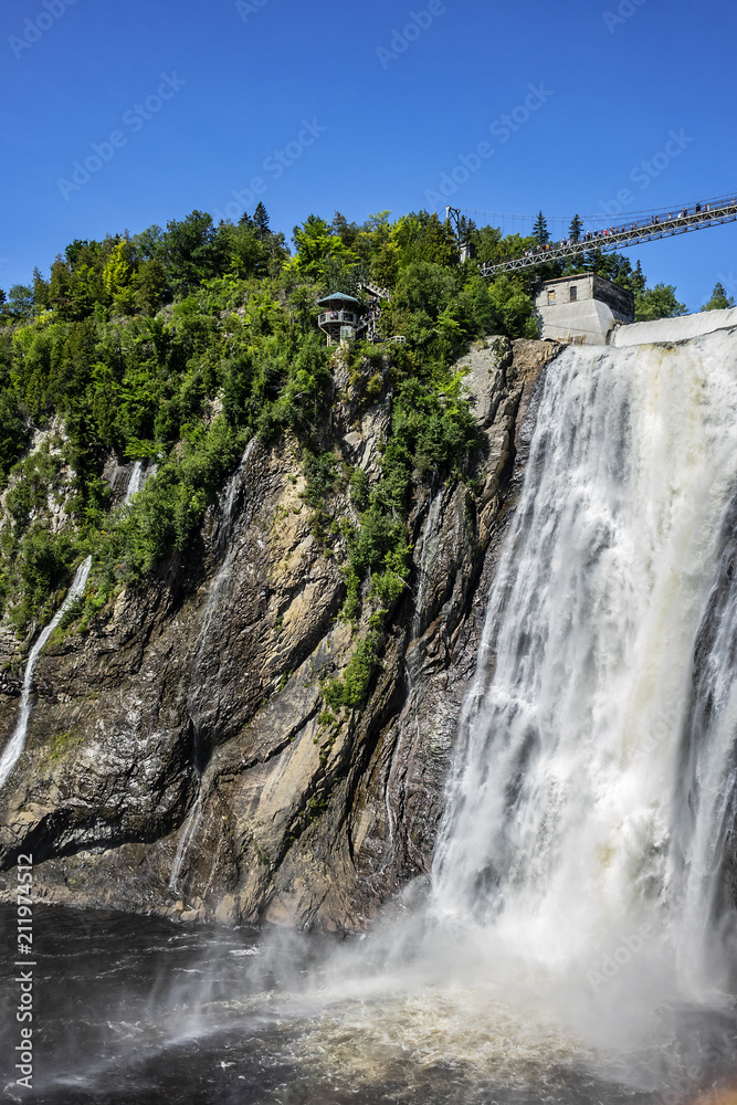 Naklejka premium The Montmorency waterfall and bridge over waterfall. Montmorency falls, located between the river and the cliffs (10 km east of Quebec City): 275 feet (83 meters) high. Quebec, Canada, North America.